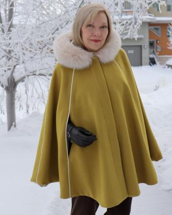 Pixie “Alyse” cape featuring a hood which is trimmed with snow top fox fur and vertical, cream, braid details.